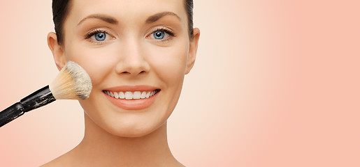 Image showing happy woman applying powder foundation with brush