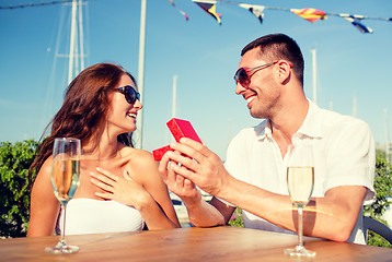 Image showing smiling couple with champagne and gift at cafe