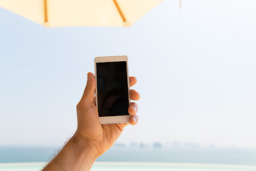 Image showing close up of male hand holding smartphone on beach