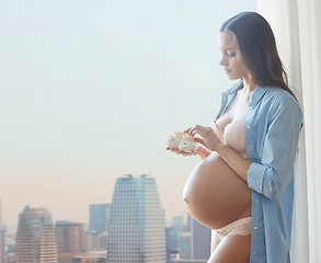 Image showing happy pregnant woman with baby booties at home