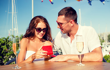 Image showing smiling couple with champagne and gift at cafe