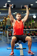 Image showing young man with dumbbells flexing muscles in gym