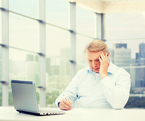 Image showing senior man with laptop and pen writing at office