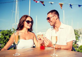 Image showing smiling couple with champagne and gift at cafe