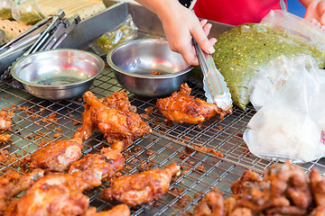 Image showing close up of cook hand with tongs grilling chicken