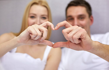 Image showing smiling couple in bed making heart shape gesture