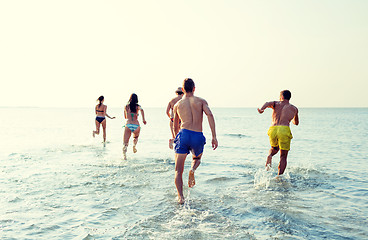 Image showing smiling friends running on beach from back