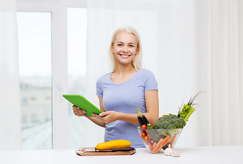 Image showing smiling young woman with tablet pc cooking at home