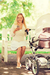 Image showing happy mother with smartphone and stroller in park