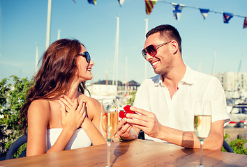 Image showing smiling couple with champagne and gift at cafe