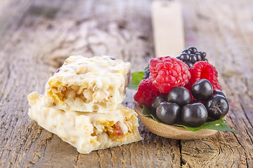 Image showing muesli bars with fresh berries in spoon on wooden