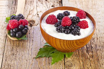 Image showing yogurt with wild berries in wooden bowl on wooden 