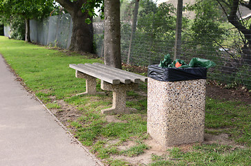 Image showing Full trash can next to empty bench