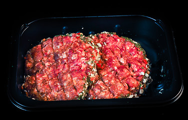 Image showing Two raw red burgers in a black plastic tray isolated on black