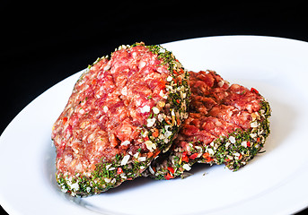 Image showing Closeup of raw red hamburgers on white plate isolated on black