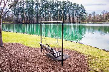 Image showing Empty wooden park bench overlooking a lake or pond