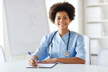 Image showing happy female doctor or nurse writing to clipboard