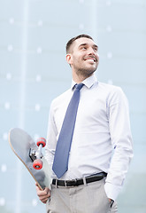 Image showing young smiling businessman with skateboard outdoors