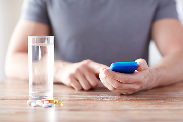 Image showing close up of hands with smartphone, pills and water