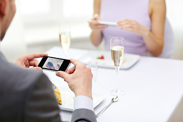 Image showing close up of couple with smartphones at restaurant