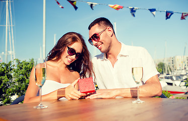 Image showing smiling couple with champagne and gift at cafe