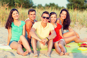 Image showing smiling friends sitting on summer beach