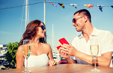 Image showing smiling couple with champagne and gift at cafe