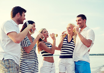 Image showing smiling friends with drinks in bottles on beach