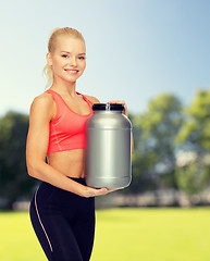 Image showing smiling sporty woman with jar of protein