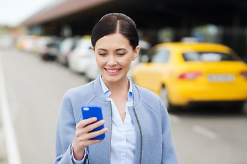 Image showing smiling woman with smartphone over taxi in city