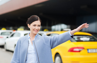 Image showing smiling young woman waving hand and catching taxi