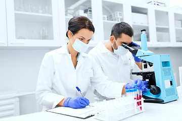 Image showing scientists with clipboard and microscope in lab