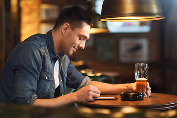 Image showing man with smartphone and beer texting at bar