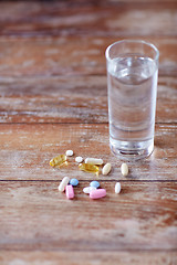 Image showing pills and capsules with glass of water on table