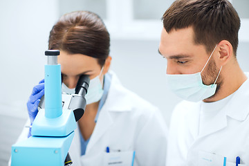Image showing scientists in masks looking to microscope at lab
