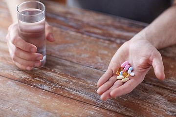 Image showing close up of male hands holding pills and water