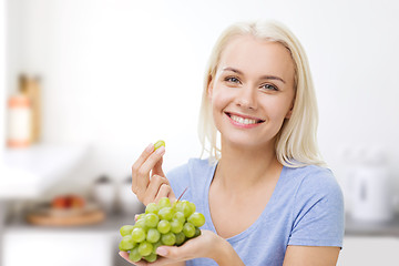 Image showing happy woman eating grapes on kitchen