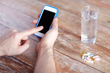 Image showing close up of hands with smartphone, pills and water