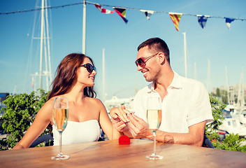 Image showing smiling couple with champagne and gift at cafe