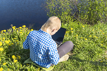 Image showing Ten year boy with laptop on riverside in summer