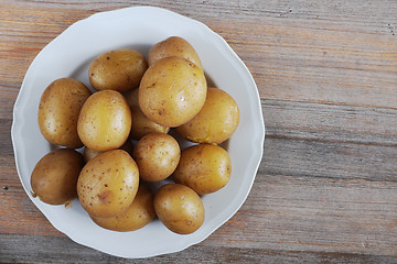 Image showing boiled potatoes in their skins on a plate, wooden background