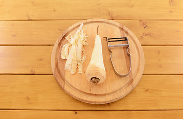 Image showing Peeled parsnip with vegetable peeler on a chopping board