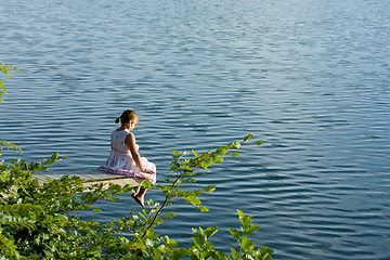 Image showing Girl in summer dress sitting at deck over water
