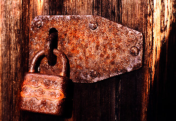 Image showing Old rusty padlock on very old weather beaten door in brownish colours.