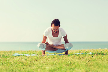 Image showing smiling man making yoga exercises outdoors