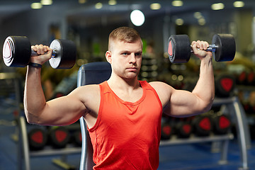 Image showing young man with dumbbells flexing muscles in gym