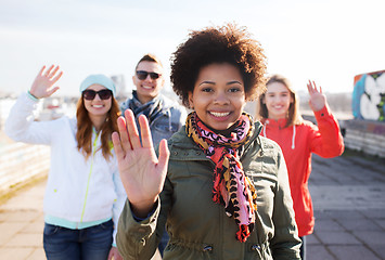 Image showing happy teenage friends waving hands on city street