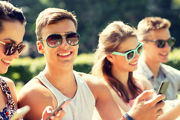 Image showing smiling friends with smartphones sitting in park