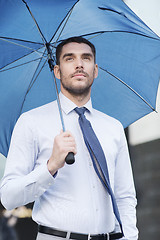 Image showing young serious businessman with umbrella outdoors