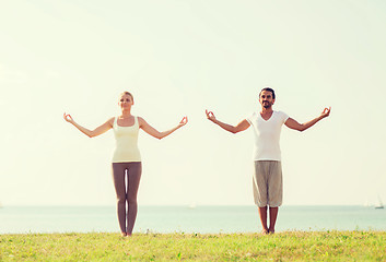 Image showing smiling couple making yoga exercises outdoors